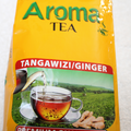 Close-up of Aroma Tea yellow bag front showing "Tangawizi/Ginger" red banner, brewed tea cup, ginger root, and tea plantation background